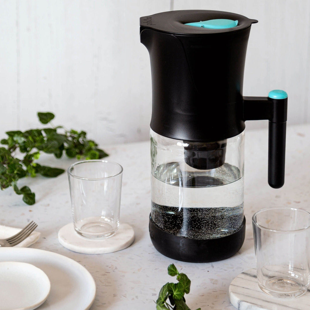 Glass Sustainable Black Water Filter Jug with refillable cartridge on marble surface with glass