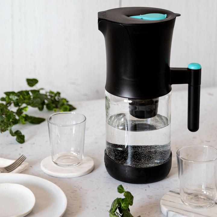Glass Sustainable Black Water Filter Jug with refillable cartridge on marble surface with glass