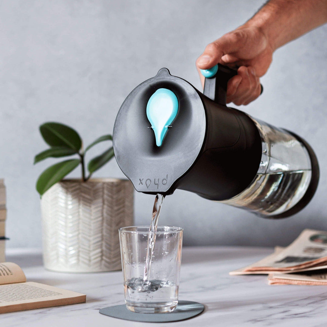 Black Sustainable Water Filter Jug with refillable cartridge pouring water into glass with plant behind