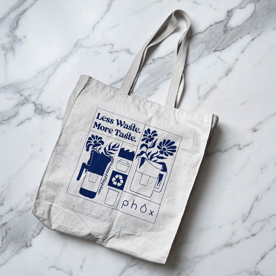 Phox Water 100% GOTS Organic Tote bag with 'Less Waste More Taste' design on a marble surface