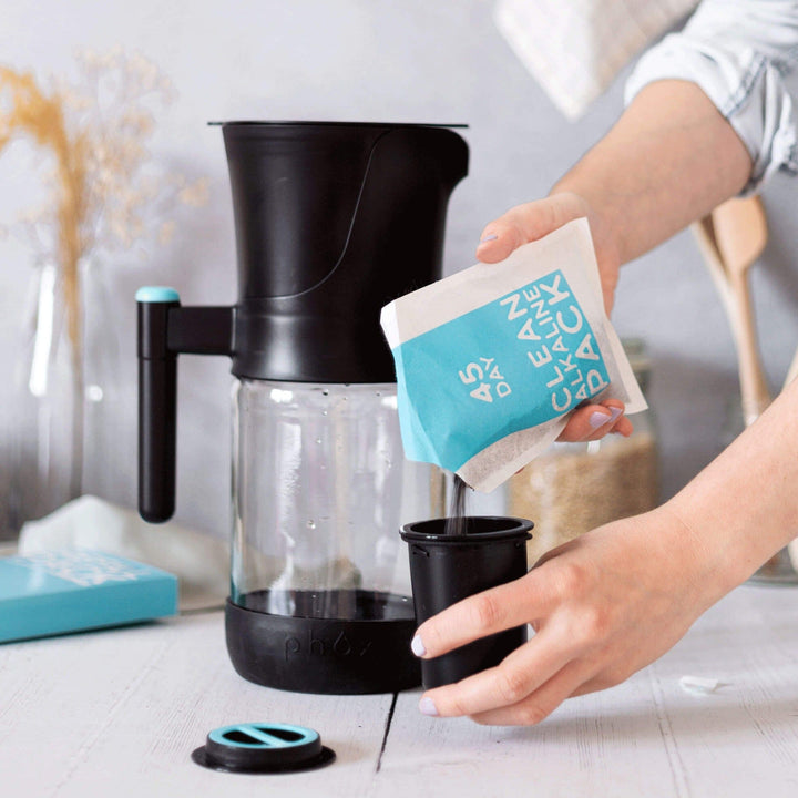 Black glass sustainable water filter jug with person pouring alkaline pack into refillable cartridge