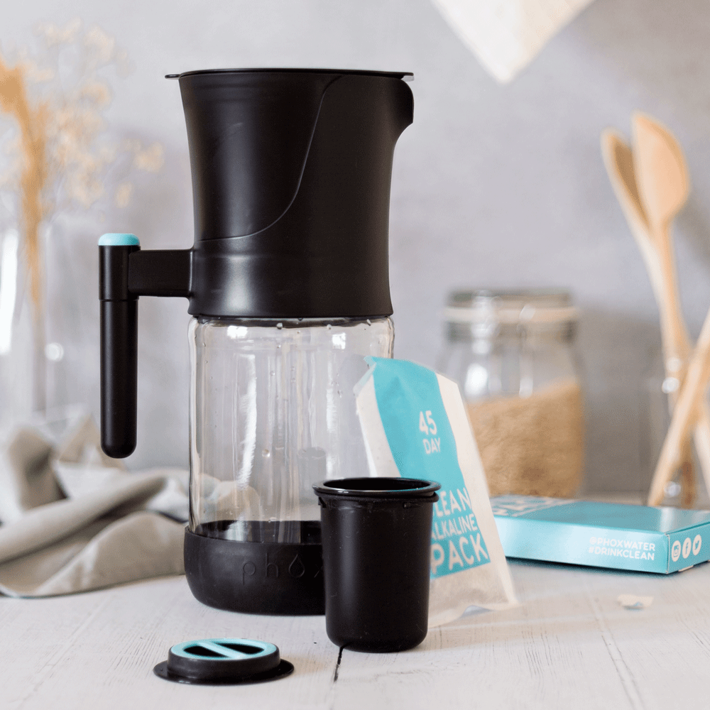 Black glass sustainable water filter jug with black refillable cartridge with alkaline pack behind